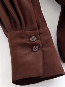 Détail de la manche d'une blouse marron foncé avec boutons doubles et plis fins