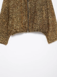 Détail de la texture à franges dorées et fermeture éclair métallique sur la veste