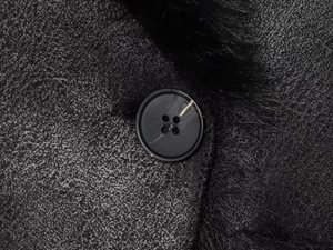 Détail d'un bouton noir sur manteau en daim gris avec doublure en fausse fourrure