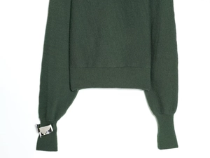 Macro detail of dark green knit sweater featuring a modern silver metal buckle on the cuff