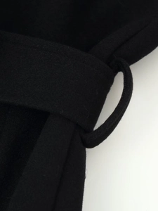 Close-up of black wool coat waist belt detail with precise stitching and soft texture