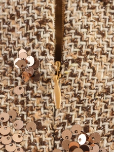 Detailed macro view of tweed fabric texture with gold sequins and a sturdy metal zipper