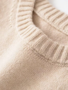 Detailed close-up of the ribbed crewneck and soft knit texture of the beige sweater