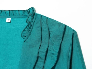 Detail view of teal knit top featuring ruffled neckline and layered pleated shoulders