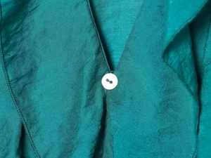 Detailed close-up of dark green silk texture with minimalist white button closure