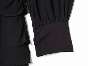 Detailaufnahme des schwarzen Langarmkleides mit gestuften Rüschen und strukturiertem Stoff