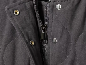 Macro detail of dark grey quilted cotton bomber jacket showing zipper and metal snap buttons