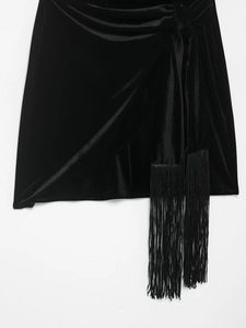 Detail of black velvet skirt with side knot and long tassel trim against white backdrop