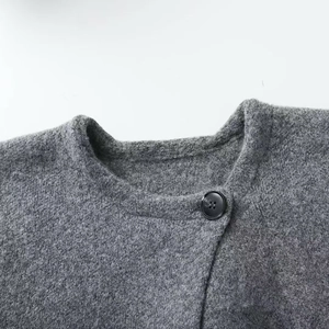 Grey knit cardigan featuring a round neckline and a black button on a minimalist backdrop
