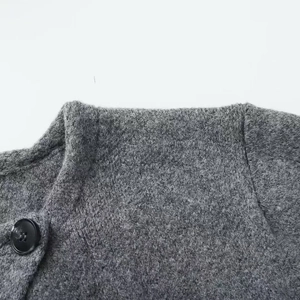 Detail of grey wool knit cardigan featuring texture, round neck and black resin button