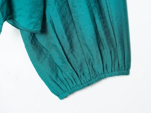 Detailed macro shot of elastic ribbed cuffs on a teal long-sleeve blouse with silk texture