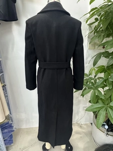 Detail view of the back of a black wool coat featuring a slim waist belt and middle slit