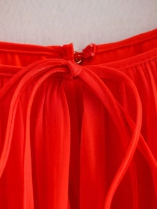 Detail of red summer dress featuring vertical pleats and a matching bow-tie waistline