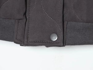 Detailed close-up of dark grey washed cotton pilot jacket with ribbed hem and snap button
