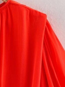 Detailed view of pleated shoulder design on bright orange summer dress fabric