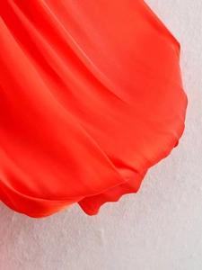 Macro shot of vibrant orange-red asymmetric hem dress with silky pleated texture
