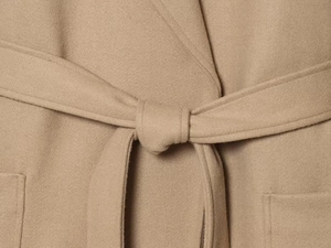 Close-up of the belted waist and textured wool fabric on a beige winter overcoat