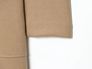Detailed macro view of camel wool coat texture and fine stitching on the sleeve cuff