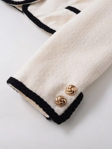 Detail of tweed jacket sleeve with golden embossed buttons and black braided trim