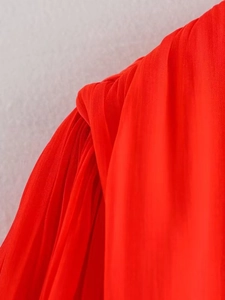 Close-up of red pleated chiffon fabric showing detailed texture and asymmetric hemline