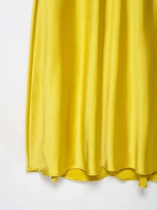Detailansicht der glatten Satin-Stofftextur und des Saums des gelben Midi-Kleides in Nahaufnahme
