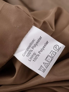 Detailed close-up of laundry care label showing 100% polyester on brown jacket