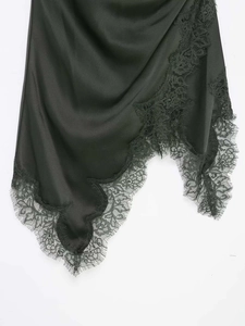 Détail d'une robe en satin vert foncé avec dentelle noire et ourlet festonné irrégulier