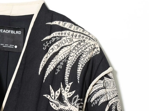 Detail of leaf embroidery on shoulder of black quilted jacket with white trim