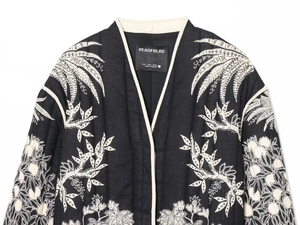 Macro detail of white floral embroidery on a black quilted jacket with brand label S