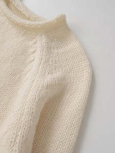 Close-up of creamy white knitted sweater featuring soft wool texture and round neckline