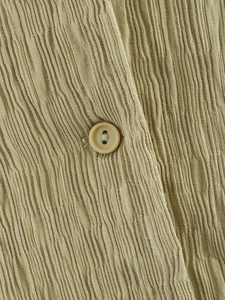 Vue macro d'un tissu texturé kaki avec plis verticaux et bouton en résine assorti