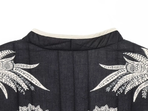 Detail of black quilted jacket featuring white leaf embroidery and refined neckline binding