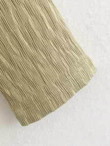 Gros plan sur le tissu texturé vert olive clair avec plis verticaux et coutures précises