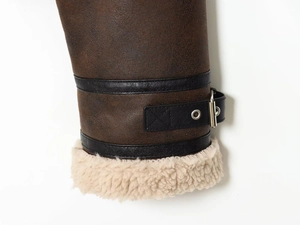 Close-up of brown suede jacket cuff with black leather straps and faux shearling lining