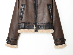 Detail of dark brown faux leather biker jacket with cream fleece lining and metal belt buckle