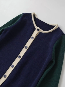 Detail of color-block knit cardigan with navy body, green sleeves and white piping