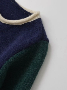 Detail of color-block knit cardigan showing dark blue and green fabric with cream trim