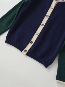 Detail of color block knit cardigan featuring navy body, green sleeves and cream trim
