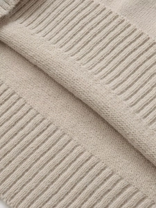 Close-up of soft beige knit sweater showing detailed plain stitch and ribbed edge texture