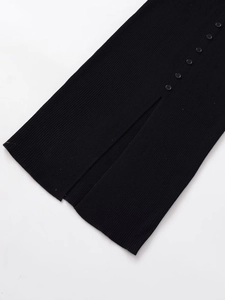 Detail view of black ribbed knit midi dress showing decorative buttons and side slit hem