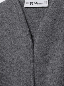 Gros plan détaillé du col en V et de l'étiquette cousue sur le cardigan gris tricoté