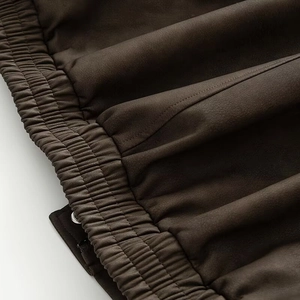 Detail of dark brown faux suede jacket featuring multi-stitched elastic hem and matte texture