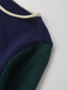 Detail of color-block knit sweater showing navy blue body and cream rolled neckline