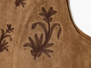 Macro shot of vintage floral embroidery on brown suede fabric of a fashion vest