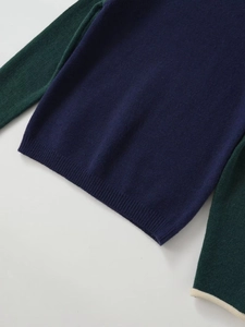 Detail of color-block knit sweater showing ribbed hem and blue-green fabric texture