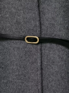 Détail d'un cardigan gris avec ceinture en cuir noir et boucle en métal doré de forme ovale