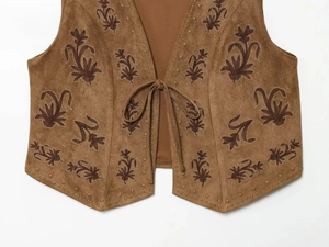 Detailed close-up of brown suede vest featuring floral embroidery and beaded trim edges