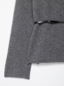 Détail d'un cardigan gris en maille avec une fine ceinture noire élégante en cuir
