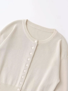 Detail of round neck beige knit cardigan with small buttons and ribbed trim edges