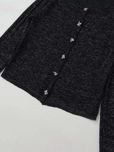 Détail de haut en maille noire avec fils argentés et boutons décoratifs en forme de nœud